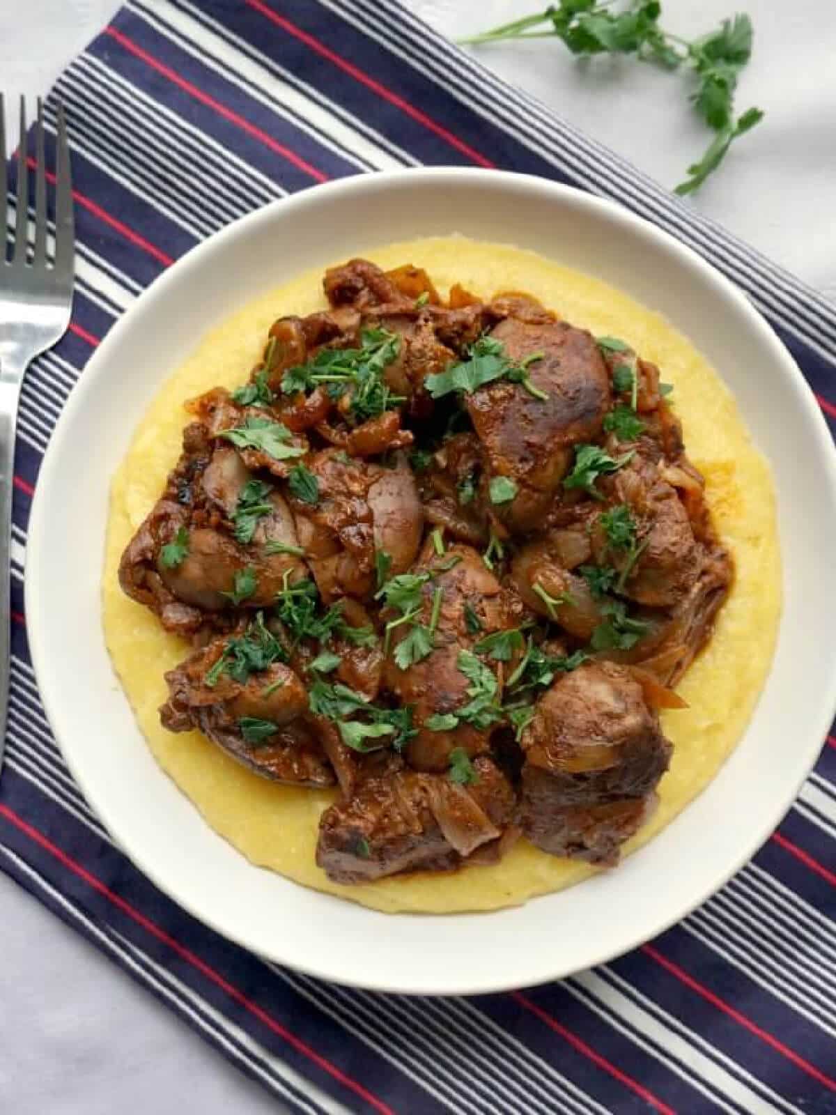 Overhead shoot of a white bowl with chicken livers over a bed of polenta.