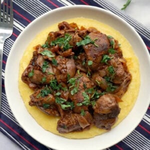 A white plate with chicken livers over a bed of polenta