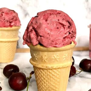 A cherry ice cream in a cone with cherries around it