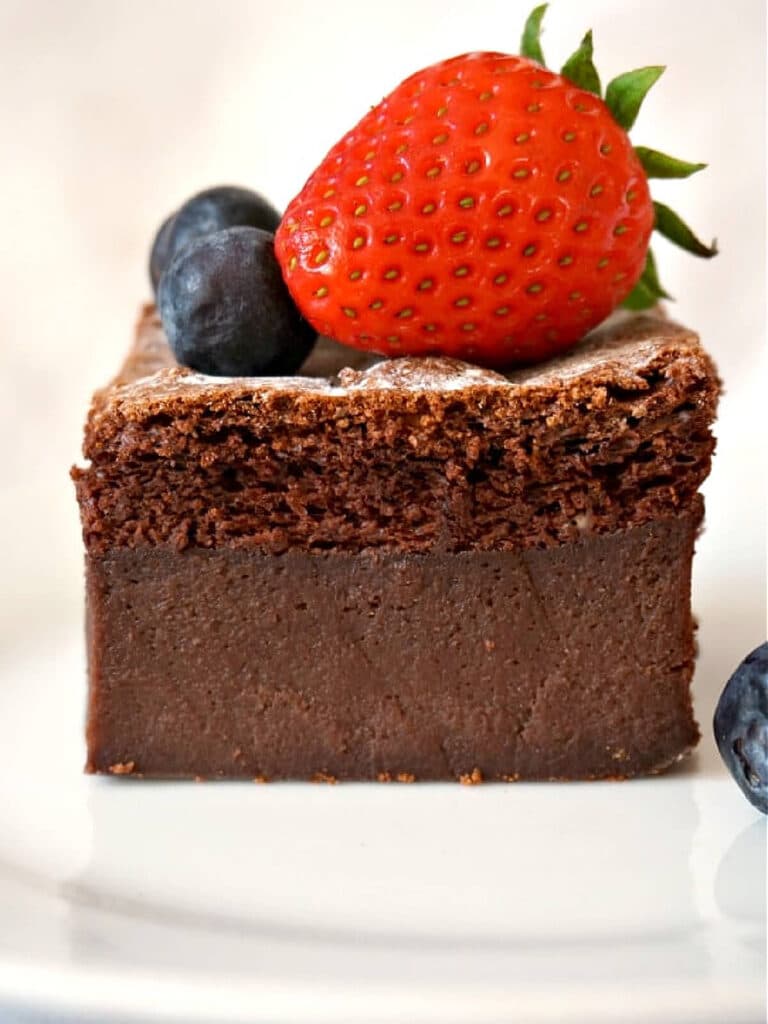 A slice of chocolate cake topped with a strawberry and 2 blueberries