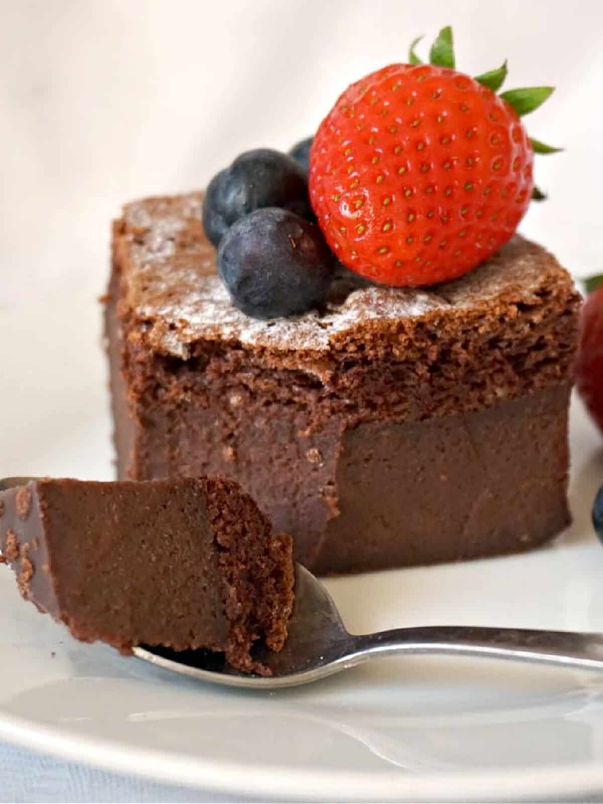 A slice of chocolate cake topped with a strawberry and 2 blueberries.