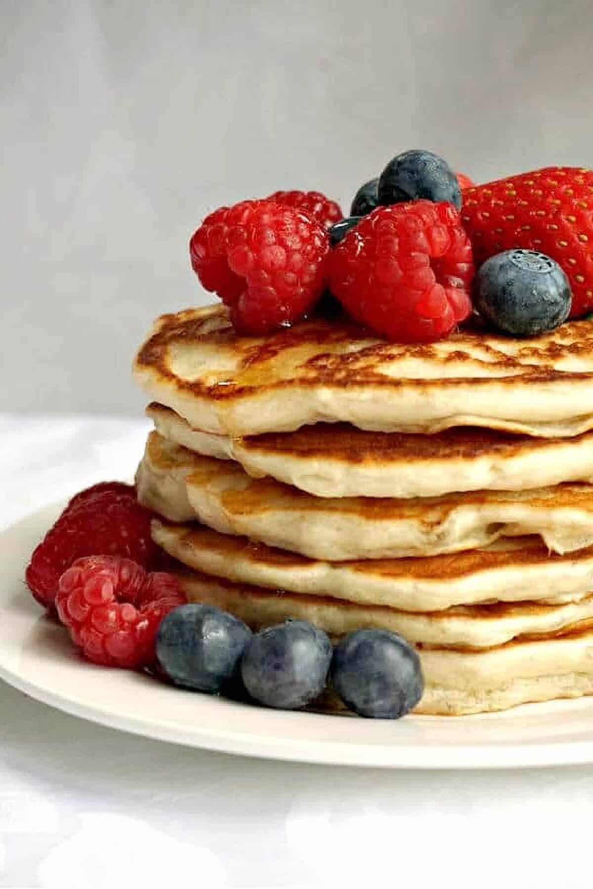 A pile of pancakes with berries around them and on top.