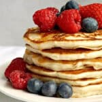 A pile of pancakes with berries on top and around them