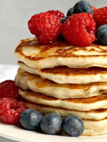 A pile of pancakes with berries on top and around them