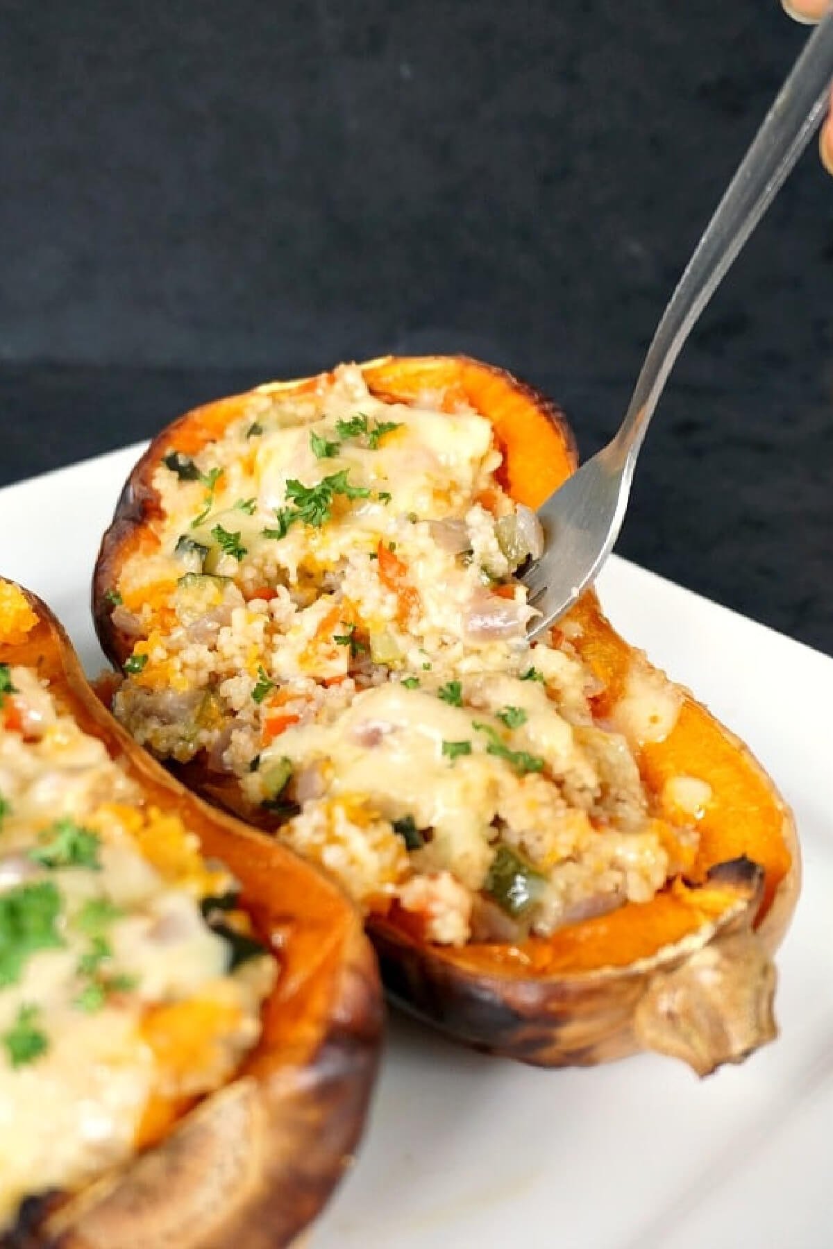 2 halves of a butternut squash stuffed with couscous and a fork in one half.