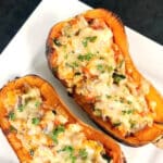 A white plate with 2 halves of a butternut squash stuffed with couscous