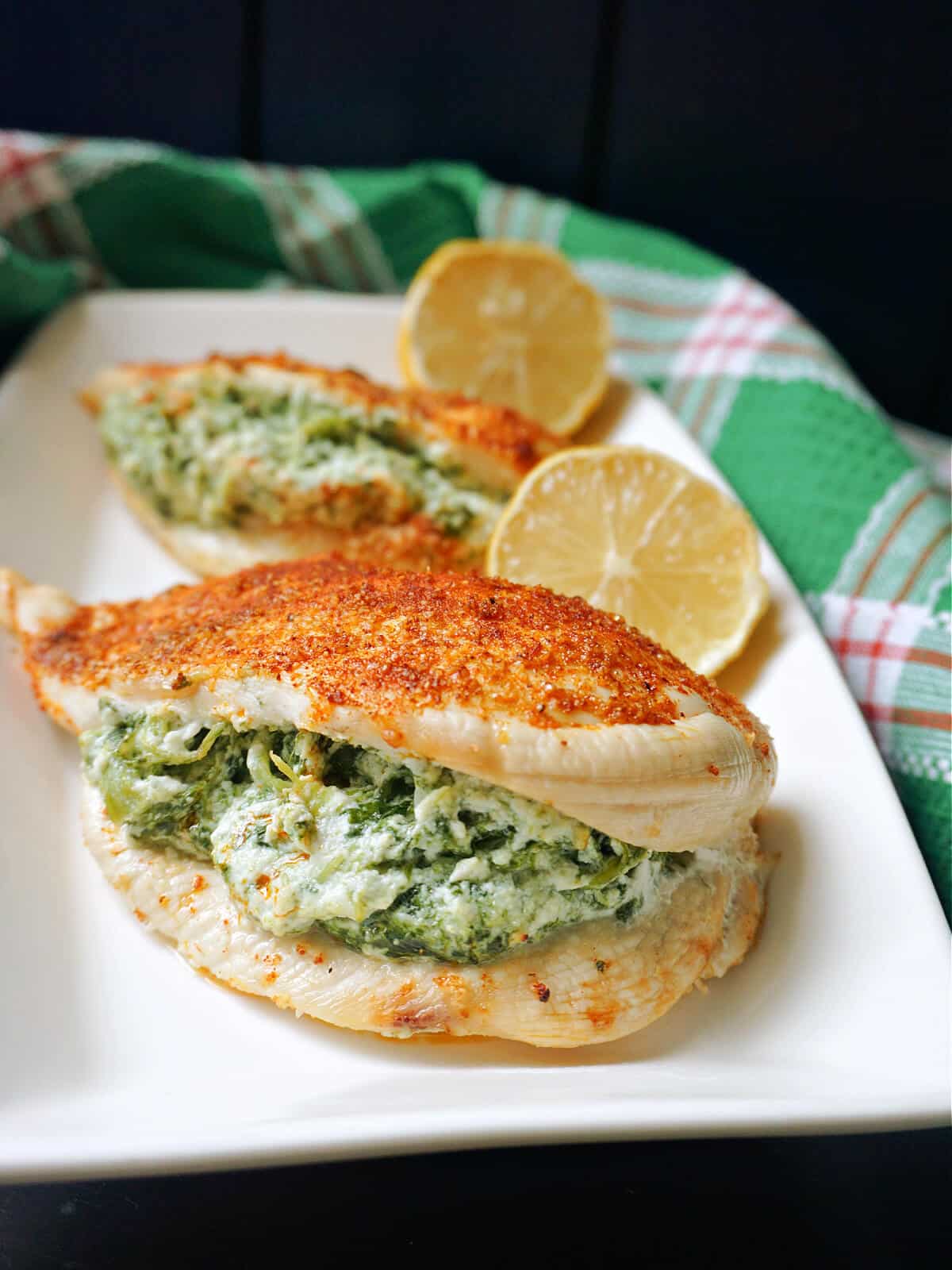 A white rectangular plate with 2 stuffed chicken breasts and 2 lemon halves