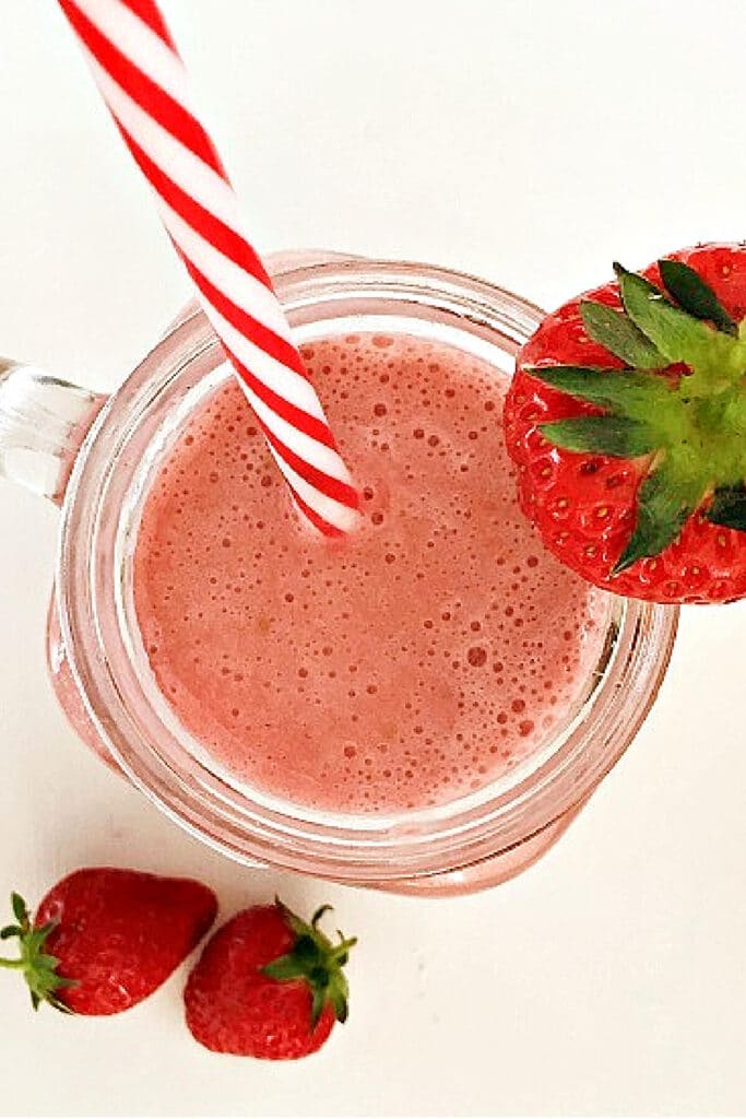 Overhead shoot of a glass with strawberry smoothie, a straw in it and a strawberry on the side