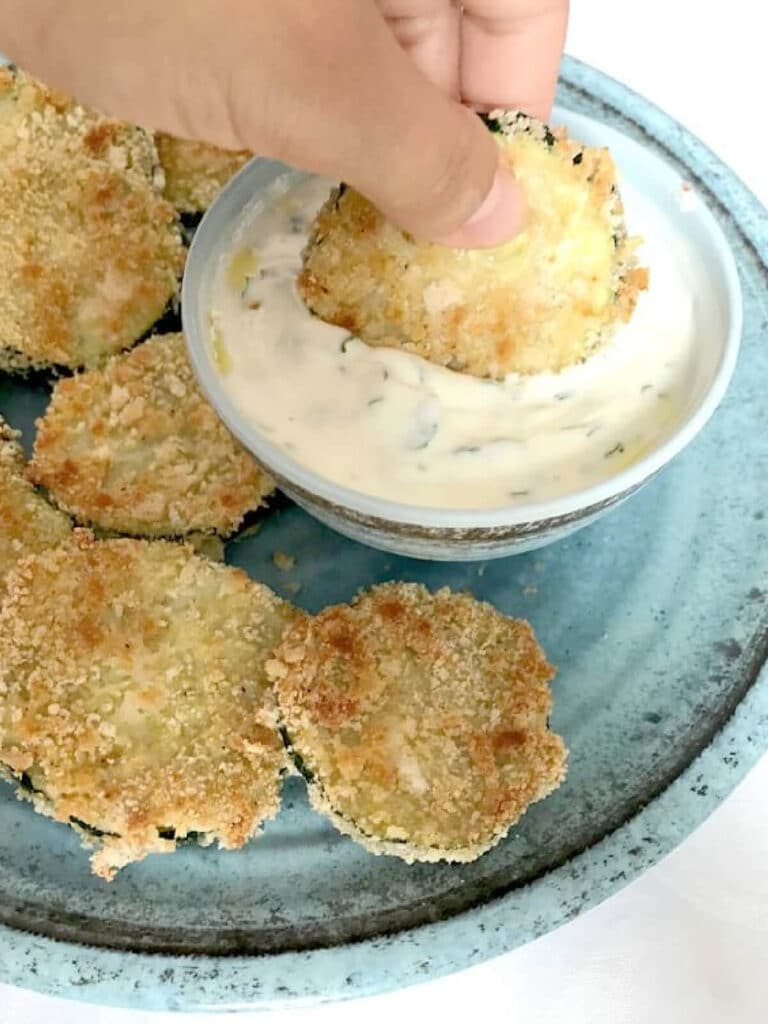 A zucchini chip being dipped into a pot of yogurt sauce