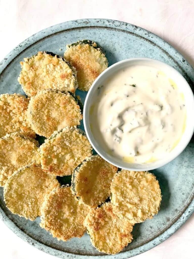 A light blue plate with zucchini chips and a pot of yogurt dip