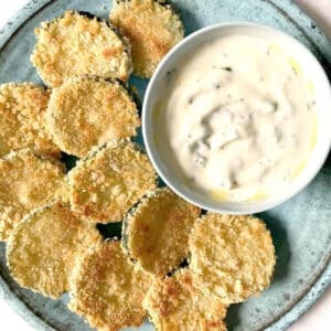 A light blue plate with zucchini chips and a pot of yogurt dip