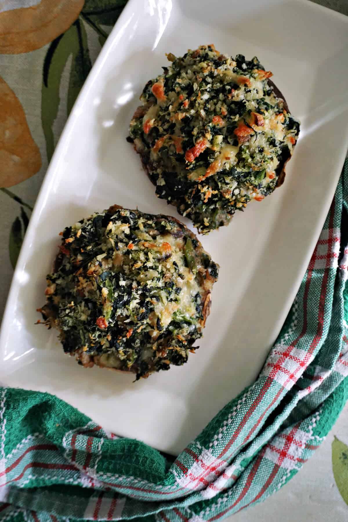 A white rectangle plate with 2 stuffed mushrooms and a tea towel around the plate.