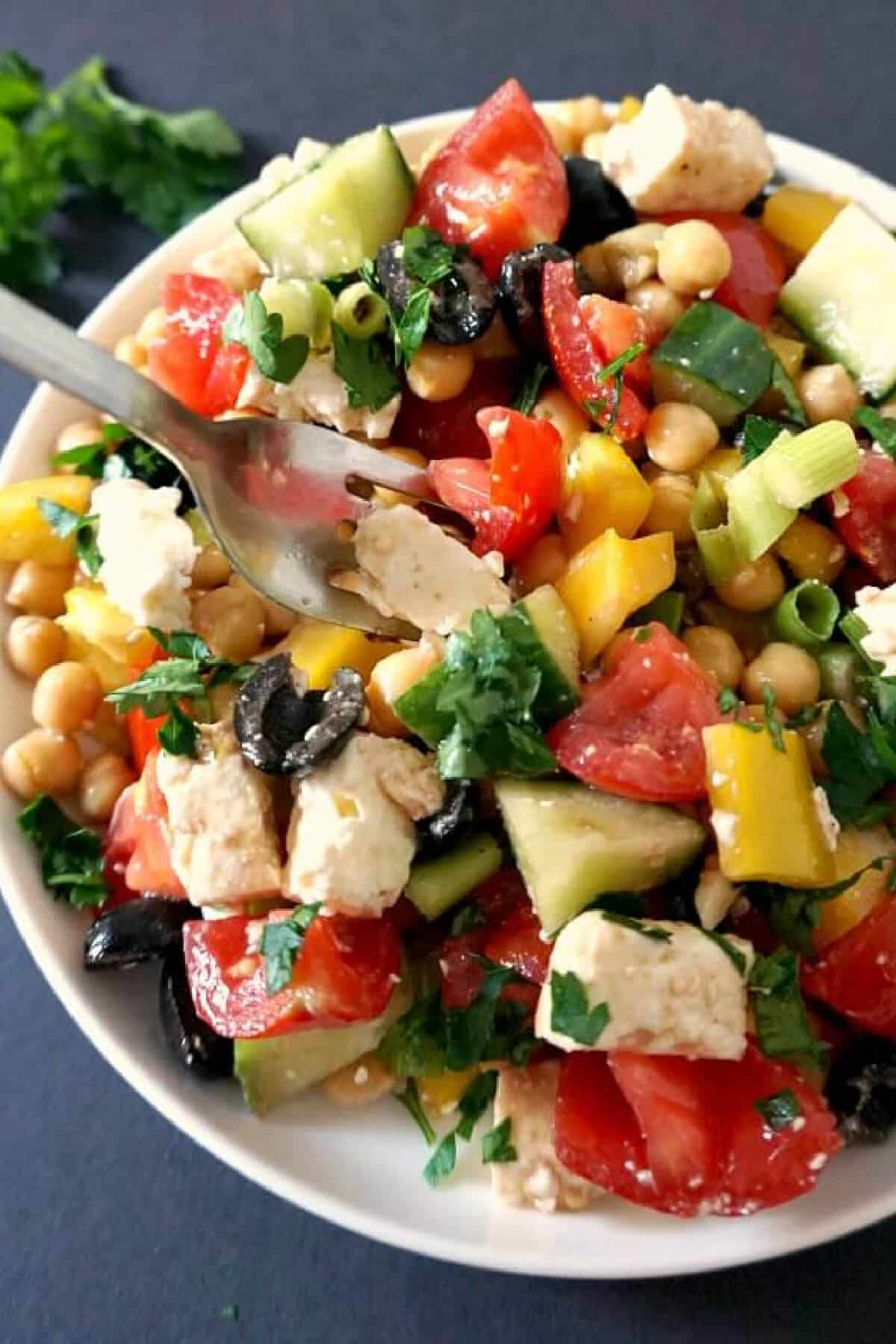 A chickpea and veggie salad in a white bowl.