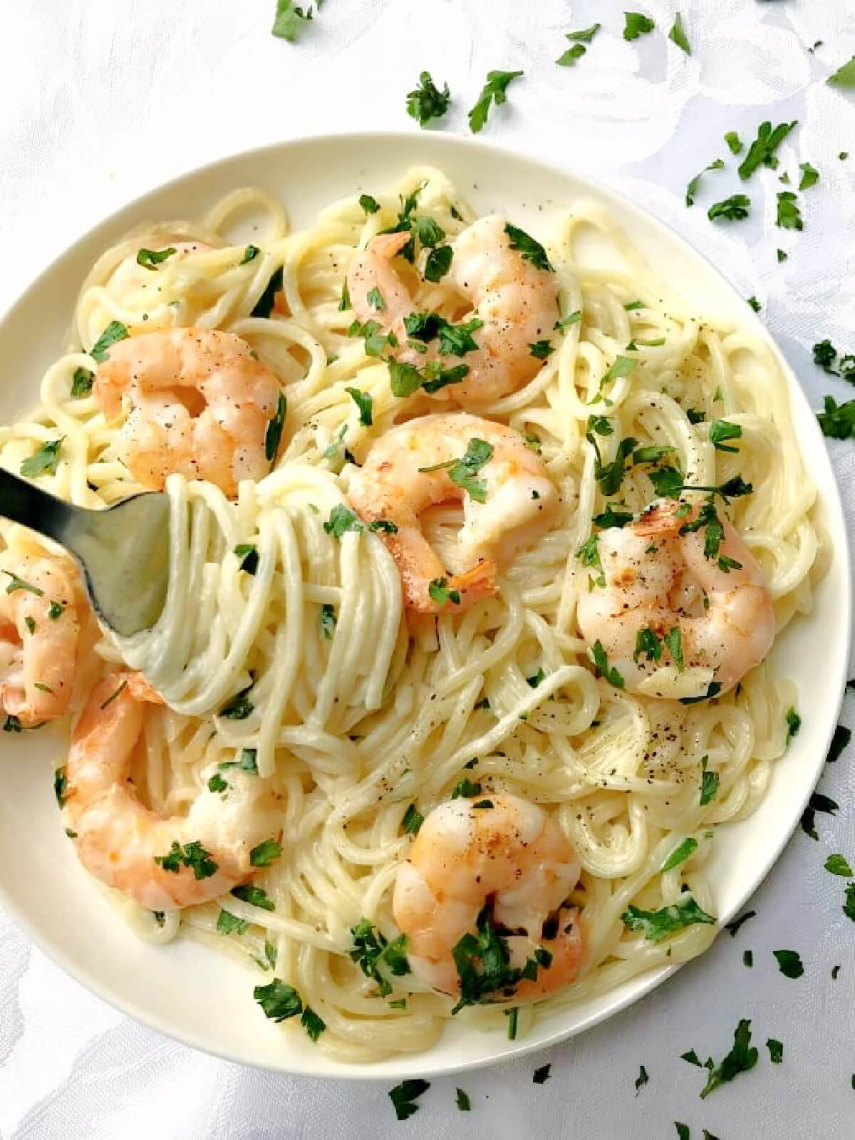A white plate with creamy spaghetti topped with prawns and chopped parsley.