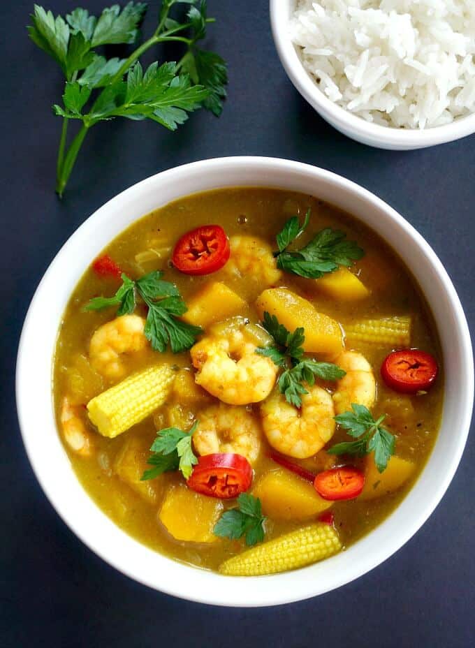 Overhead shoot of a bowl of coconut shrimp curry, a small bowl of rice and a sprig of fresh parsley