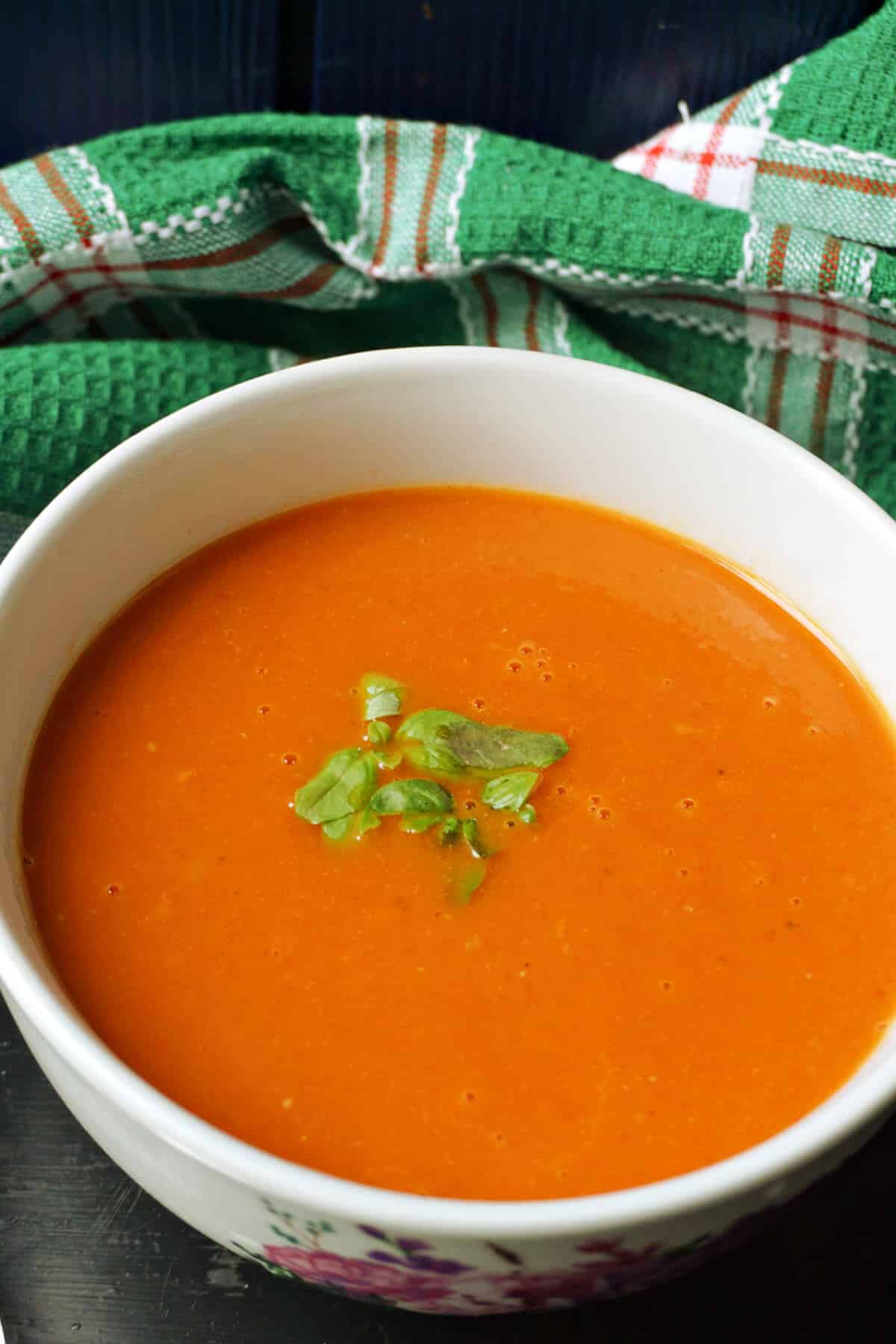 A bowl of creamed tomato soup with fresh basil leaves on top.