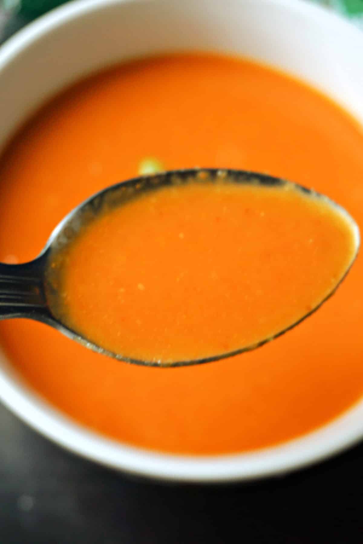 A spoonful of tomato soup over a bowl of more soup.
