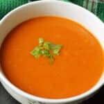 A white bowl with creamed tomato soup garnished with basil.