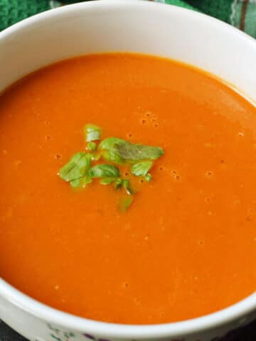 A white bowl with creamed tomato soup garnished with basil.