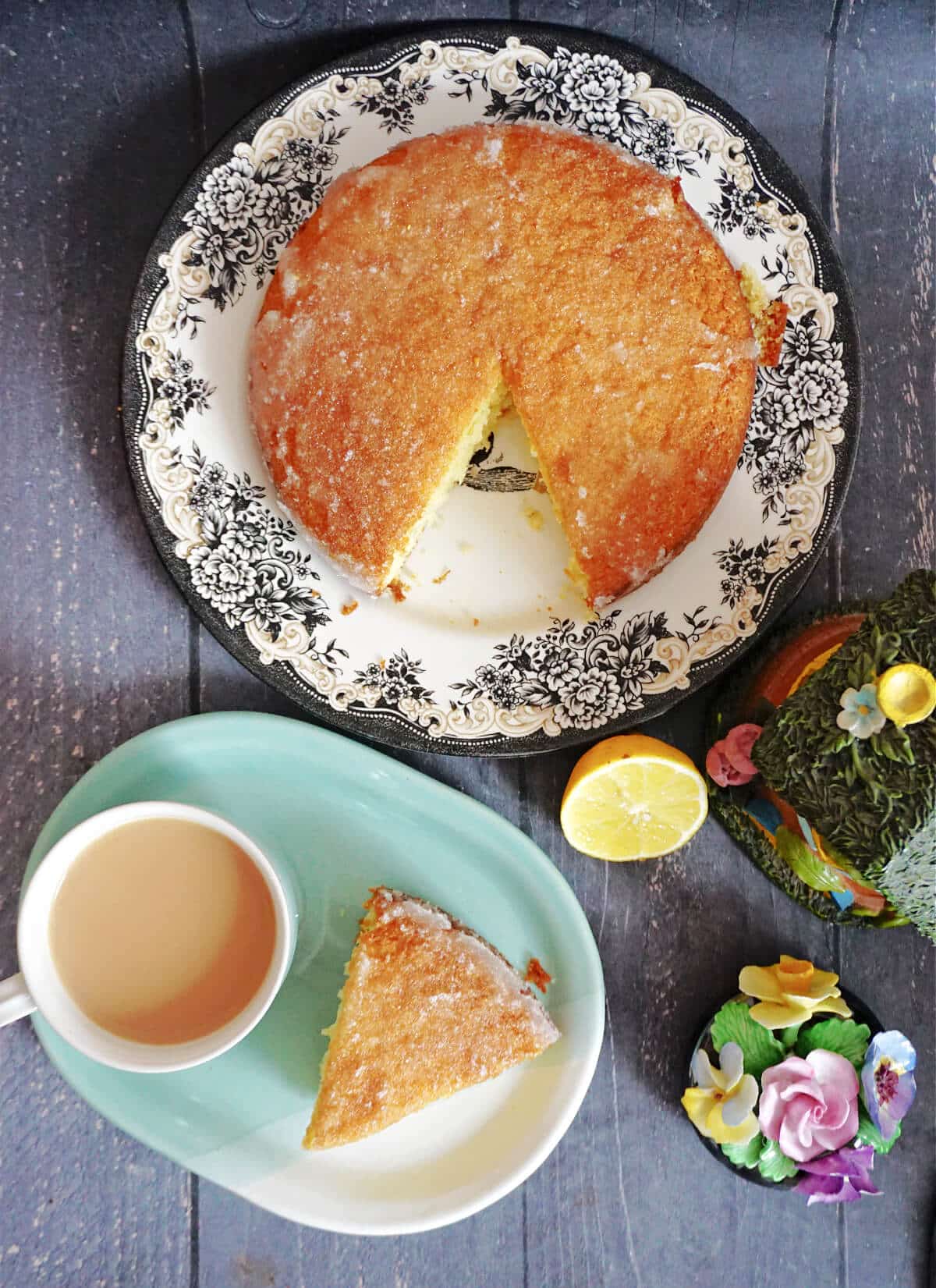 Overhead shoot of a plate with lemon drizzle cake, another plate with a cup of tea and a slice of cake, and some decorations around