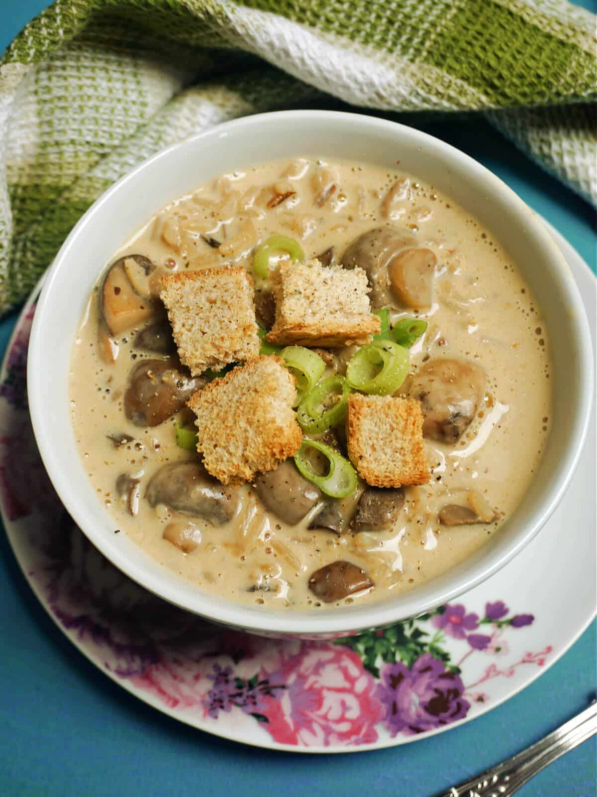 A white bowl with mushroom and wild rice soup garnished with croutons and chopped spring onions.
