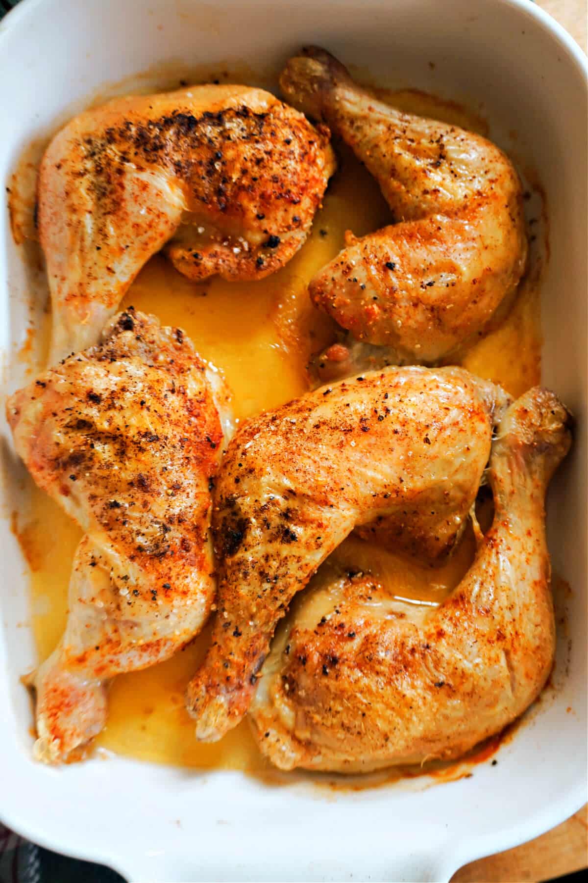 A white pan with 5 baked chicken leg quarters.
