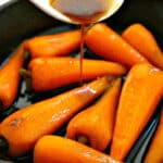 A skillet with baby carrots and a glaze being poured over them