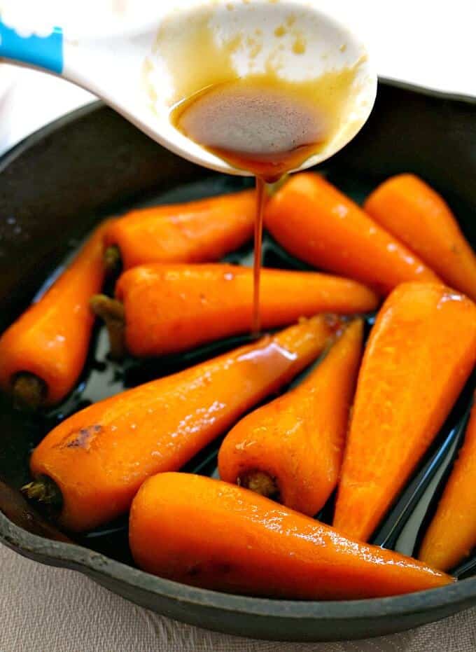 A skillet with Soy Honey Glazed Baby Carrots and glazed being drizzled over them.