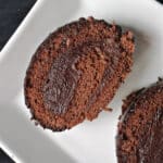 A white plate with a slice of chocolate swiss roll.