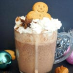 A glass with gingerbread hot chocolate topped with cream, a gingerbread man and a star anise