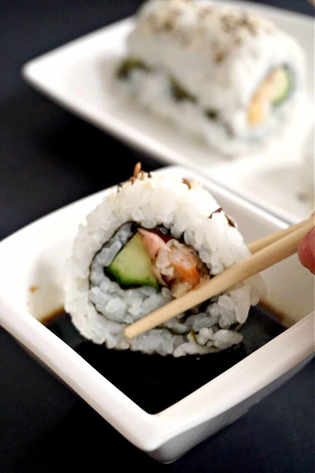 A sushi roll being dipped into sauce.