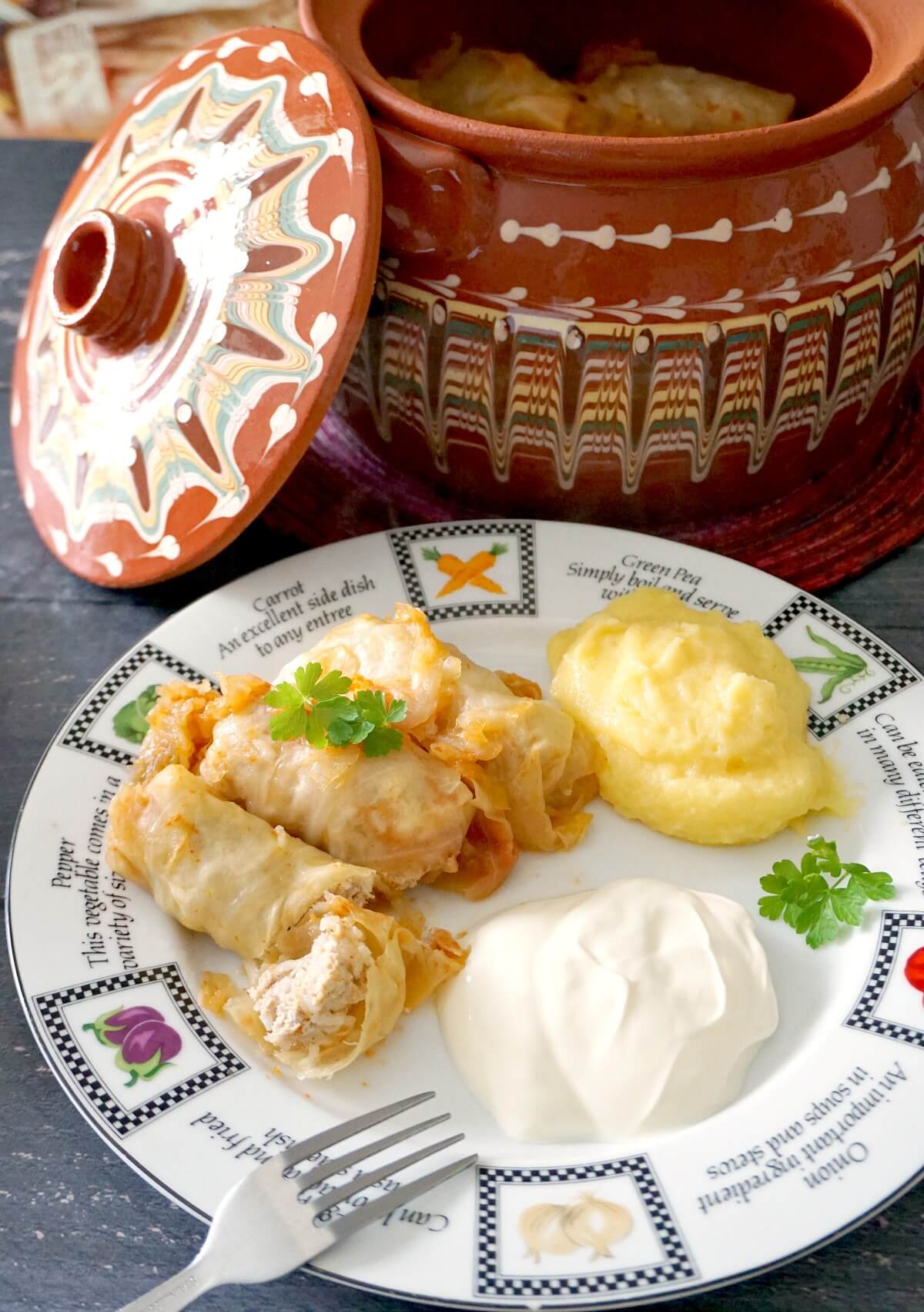 A plate with 3 cabbage rolls, polenta and sour cream and a pot of sarmale in the background