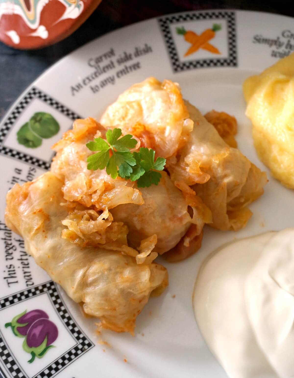 Overhead shoot of 3 cabbage rolls on a white plate with sour cream and polenta.