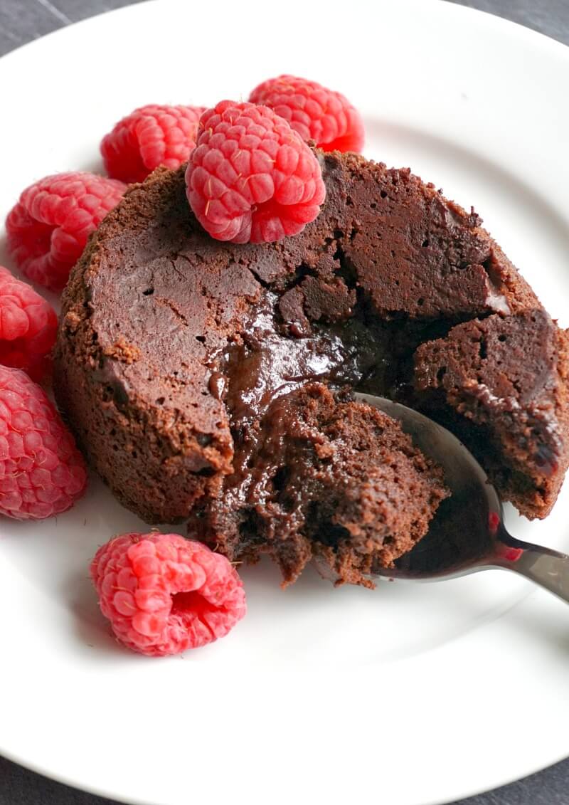 An individual chocolate lava cake with raspberries on a white plate