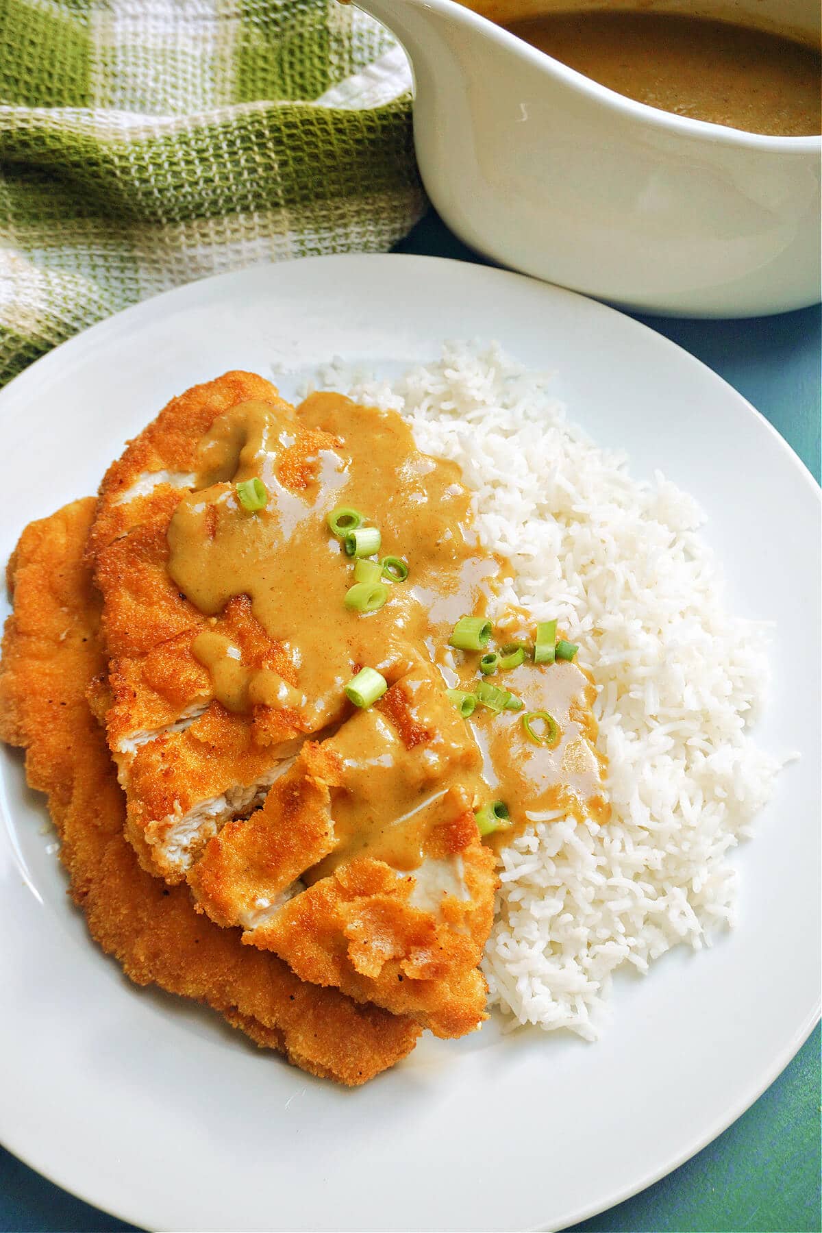 A white plate with a chicken cutlet smothered in sauce over a bed of rice.