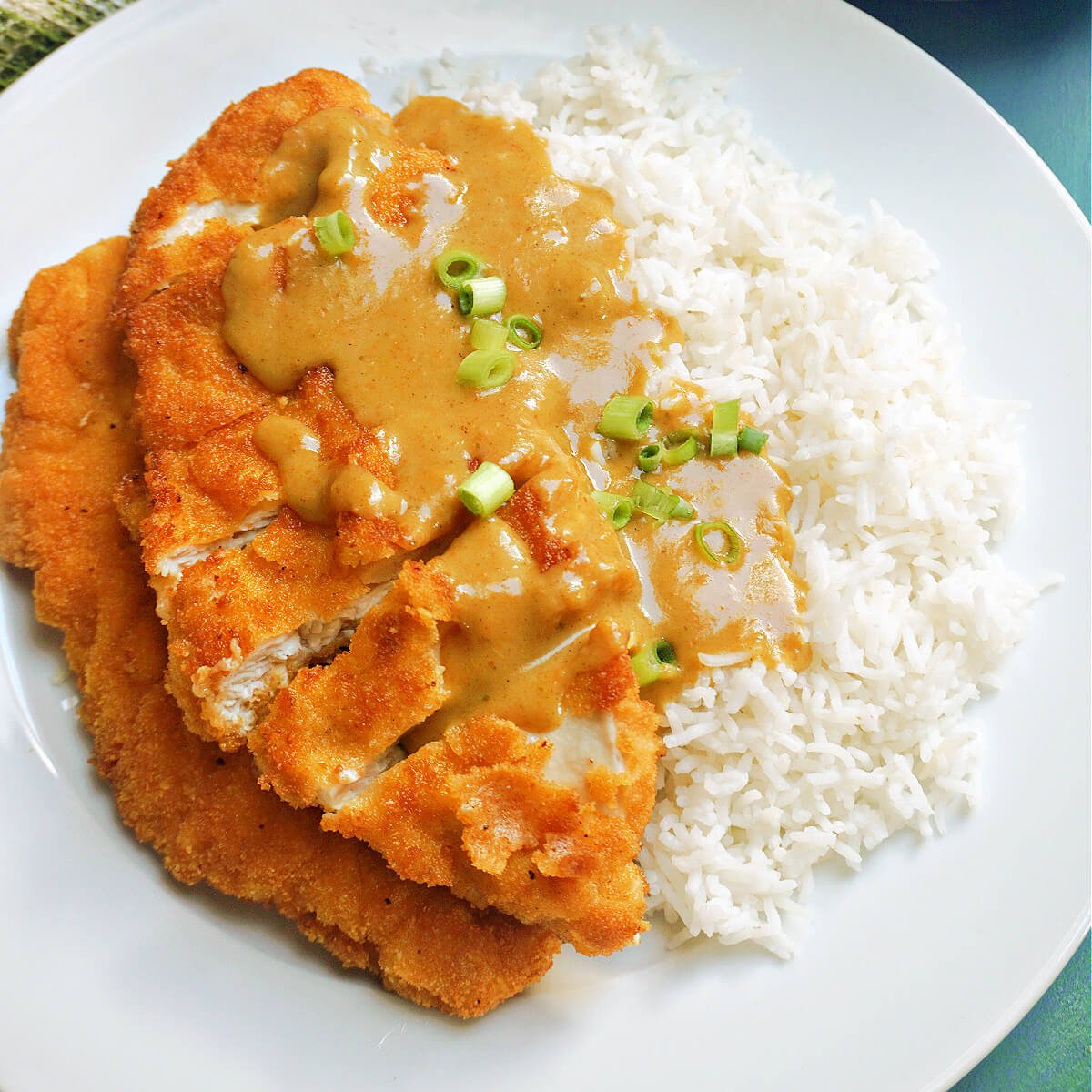 A white plate with chicken katsu in a curry sauce over a bed of rice