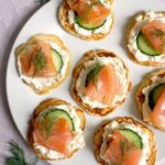Overhead shot of a white round plate with 7 smoked salmon blini canapes