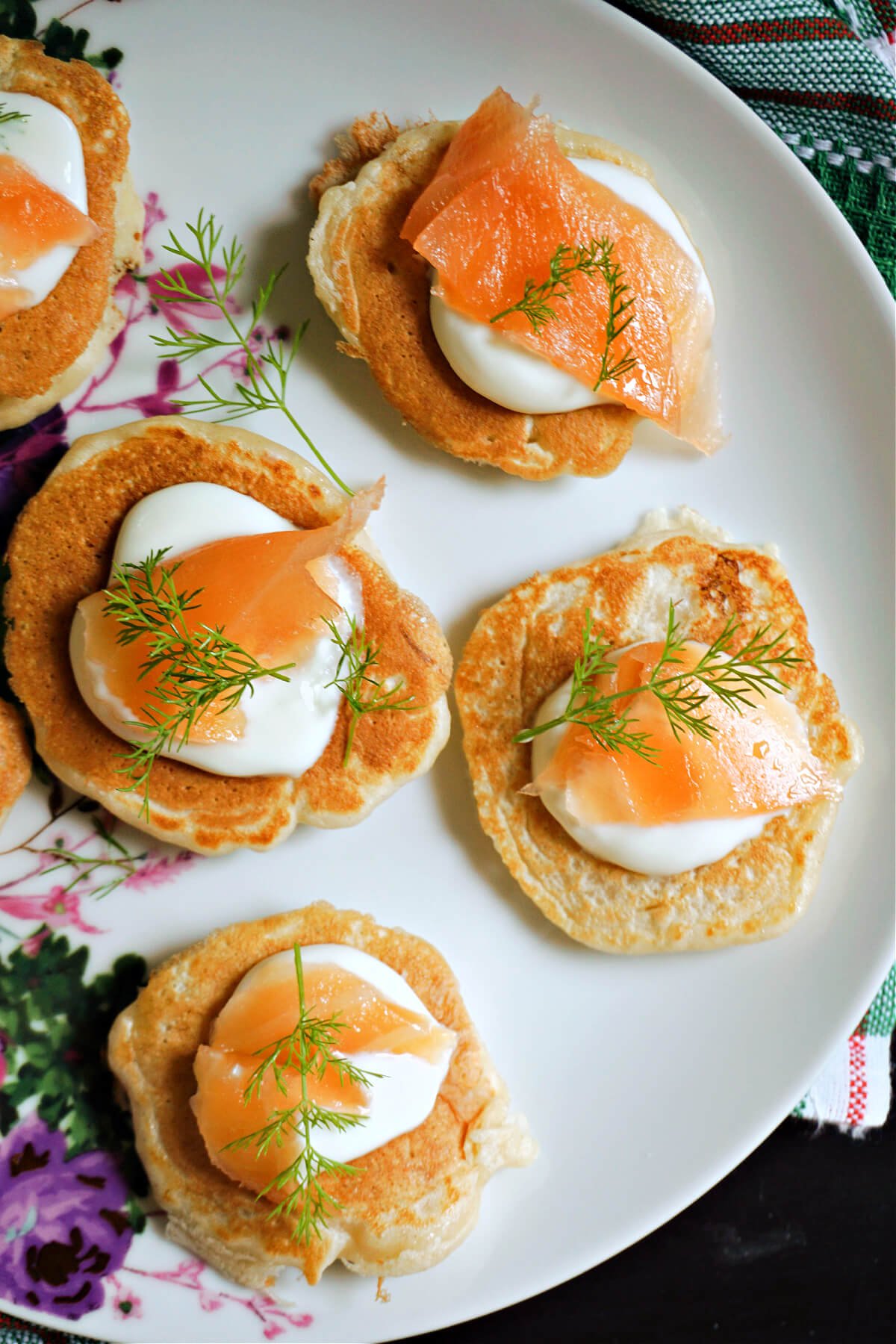 Overhead shoot of a white plate with 5 blinis topped with cream, smoked salmon and dill.