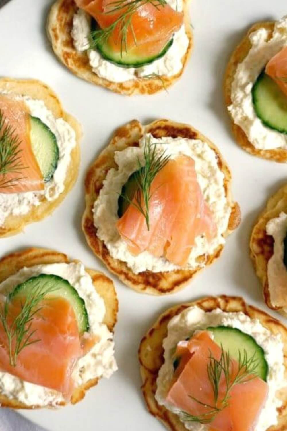 Smoked Salmon Blini Canapés, the perfect party food for your Christmas or New Year's Eve dinner, or any other party around the year. Delicious homemade blinis topped with silky cream, cucumber, smoked salmon and a touch of lemon; can't think of a better appetizer! These blinis are very easy to make, and can be topped with anything else that takes your fancy. #blinis, #canapes, #christmasfood, #newyearseveparty
