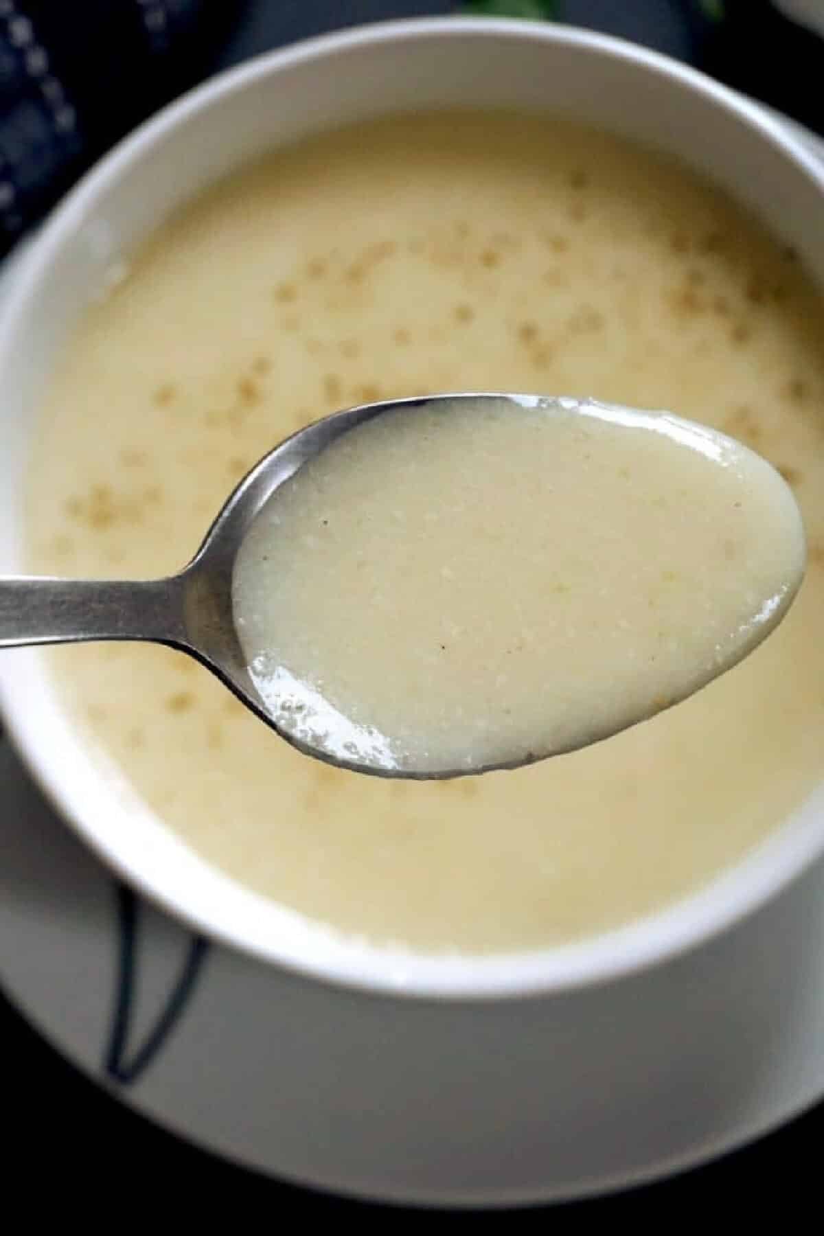 A spoonful of garlic soup over a bowl with more soup.
