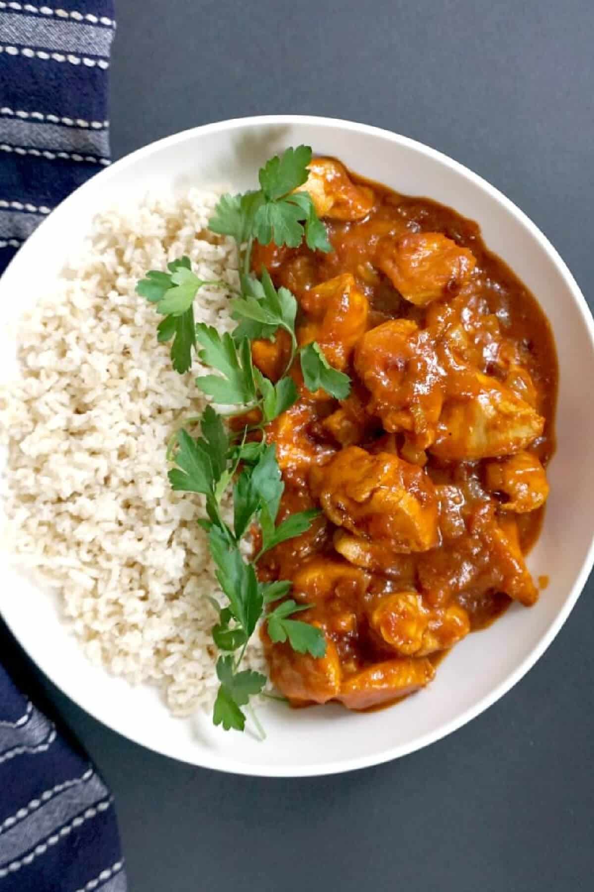 Overhead shoot of a white bowl with rice and chicken curry garnished with parsley leaves