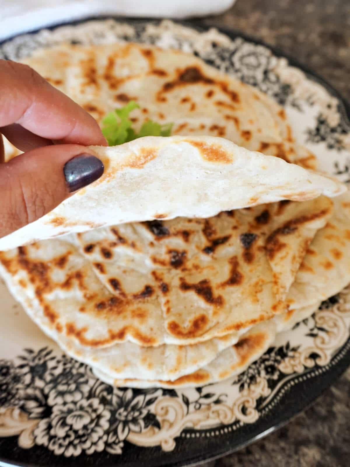 Hand-held flatbread to show how thin it is with more flat breads in the background.