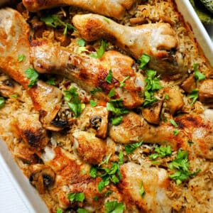 An oven dish with chicken drumsticks, rice and mushrooms, garnished with parsley.