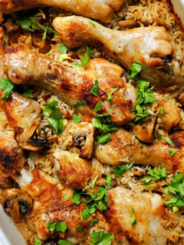 An oven dish with chicken drumsticks, rice and mushrooms, garnished with parsley.