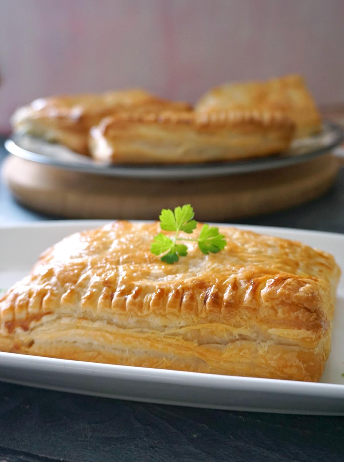 A pasty on a white plate with other 3 pasties in the background.