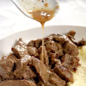 Diced beef in a white plate with gravy being poured over it