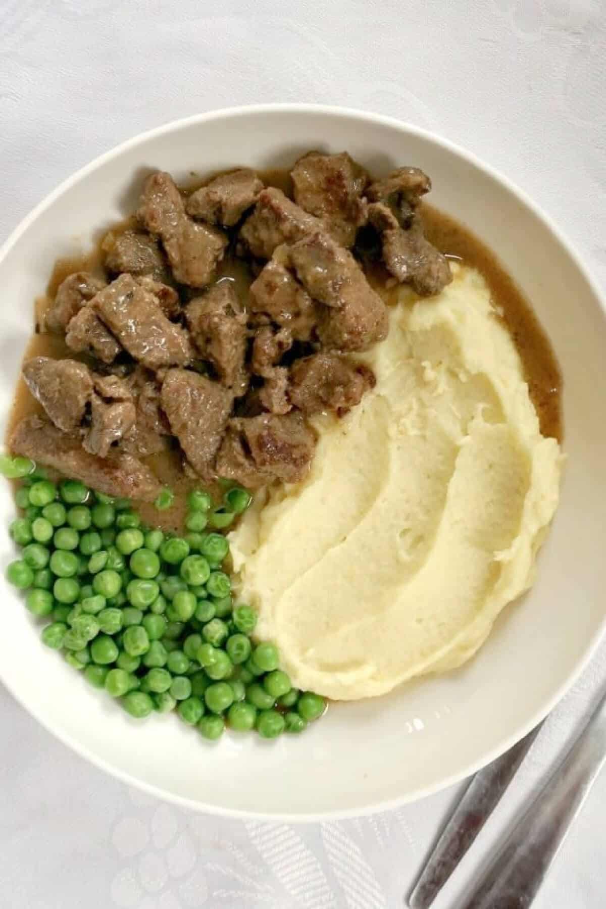 Overhead shoot of a white plate with peas, mash and beef in gravy.