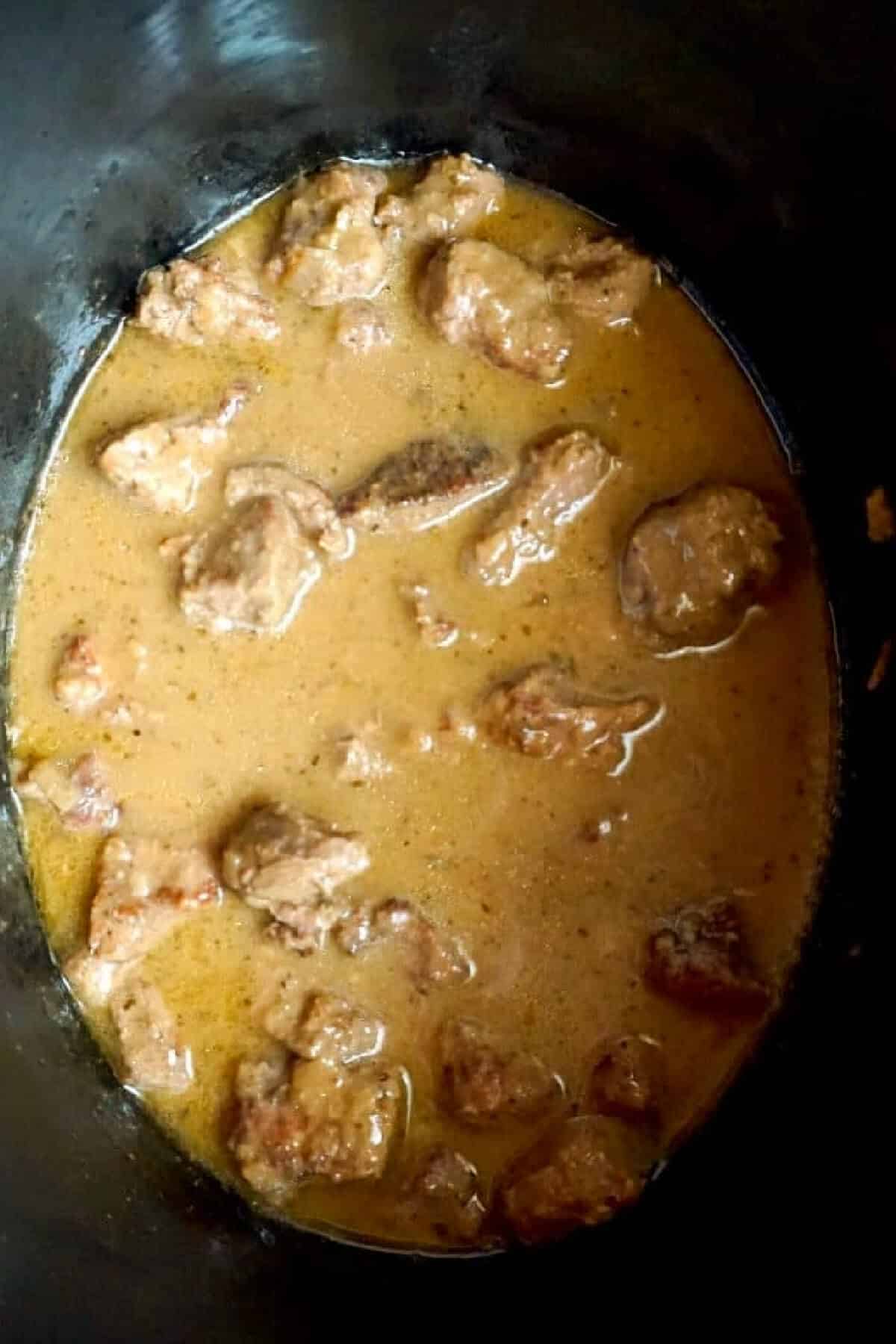 A slow cooker with diced beef in gravy.