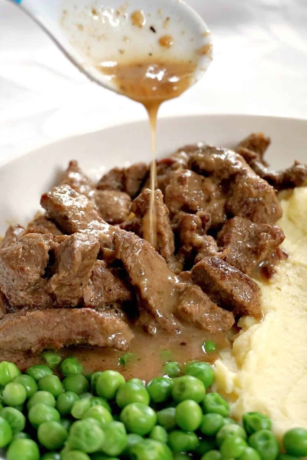 A white plate with beef tips with gravy being poured over it.