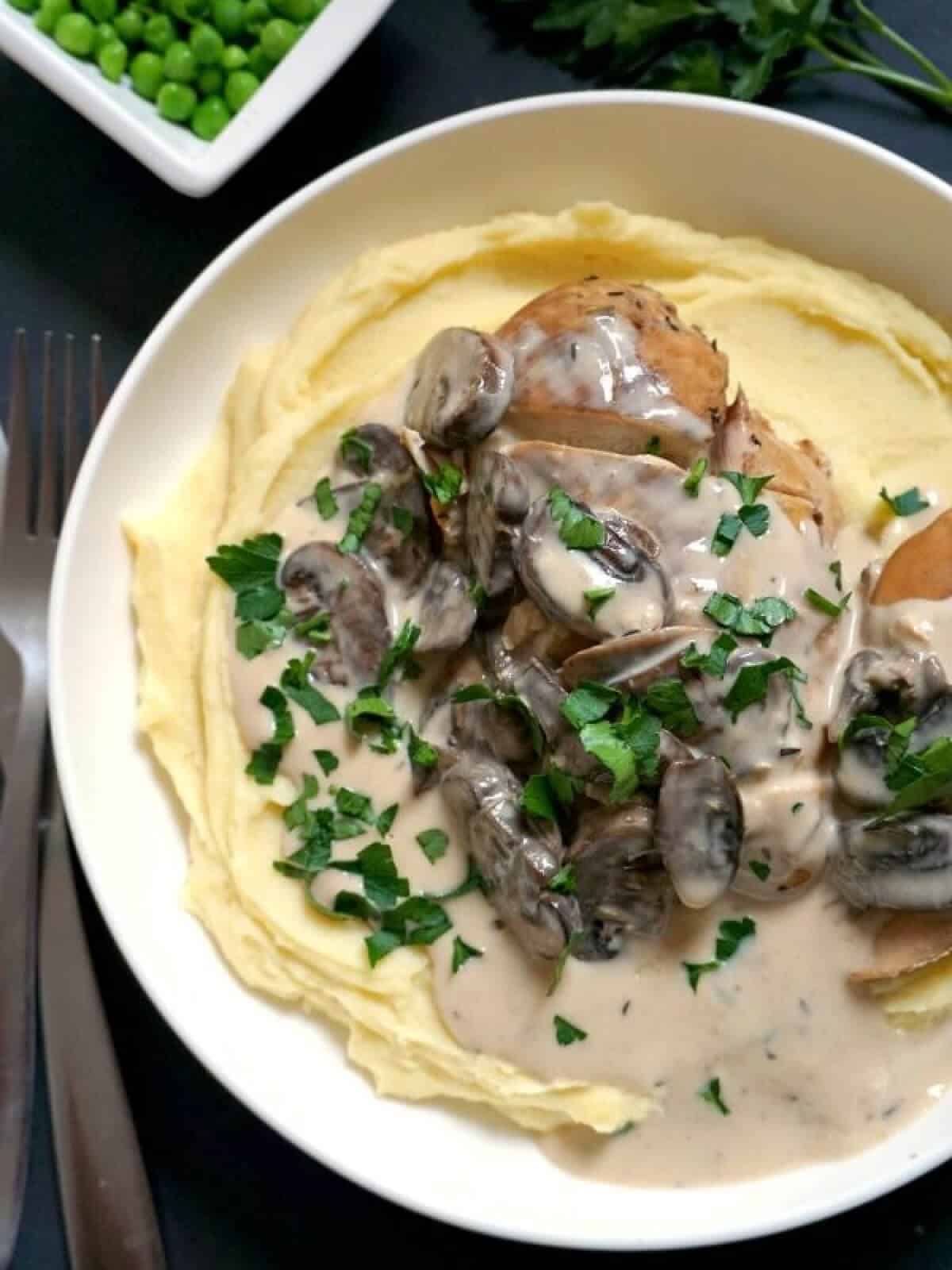 A white bowl with creamy chicken over a bed of mash.